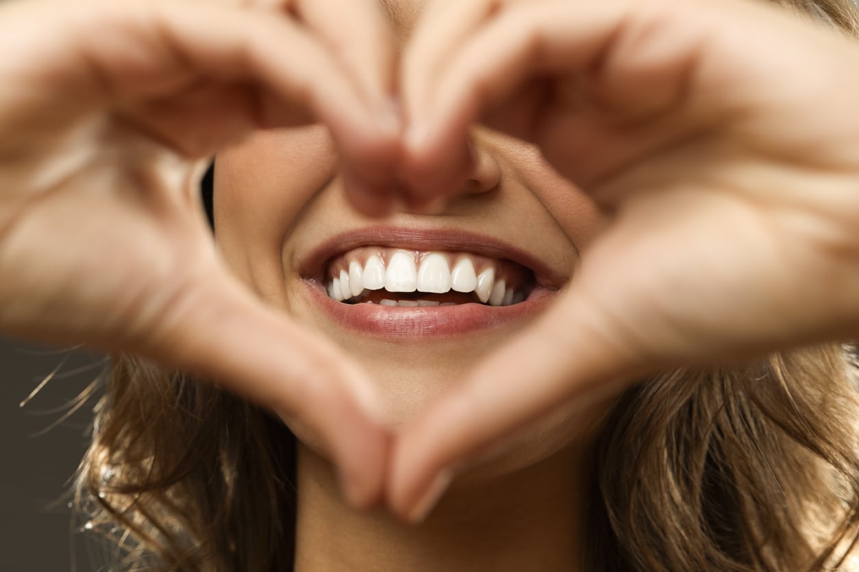 Smiling woman with bright white teeth making a heart shape with her hands – Coastal Smiles professional teeth whitening